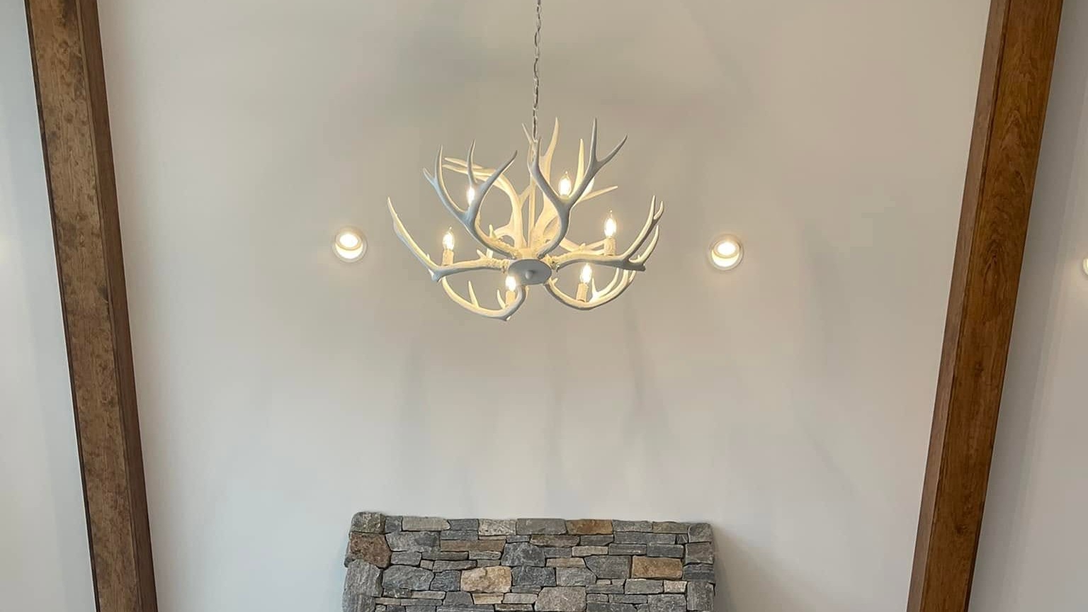 Antler chandelier wired above a stone fireplace chimney