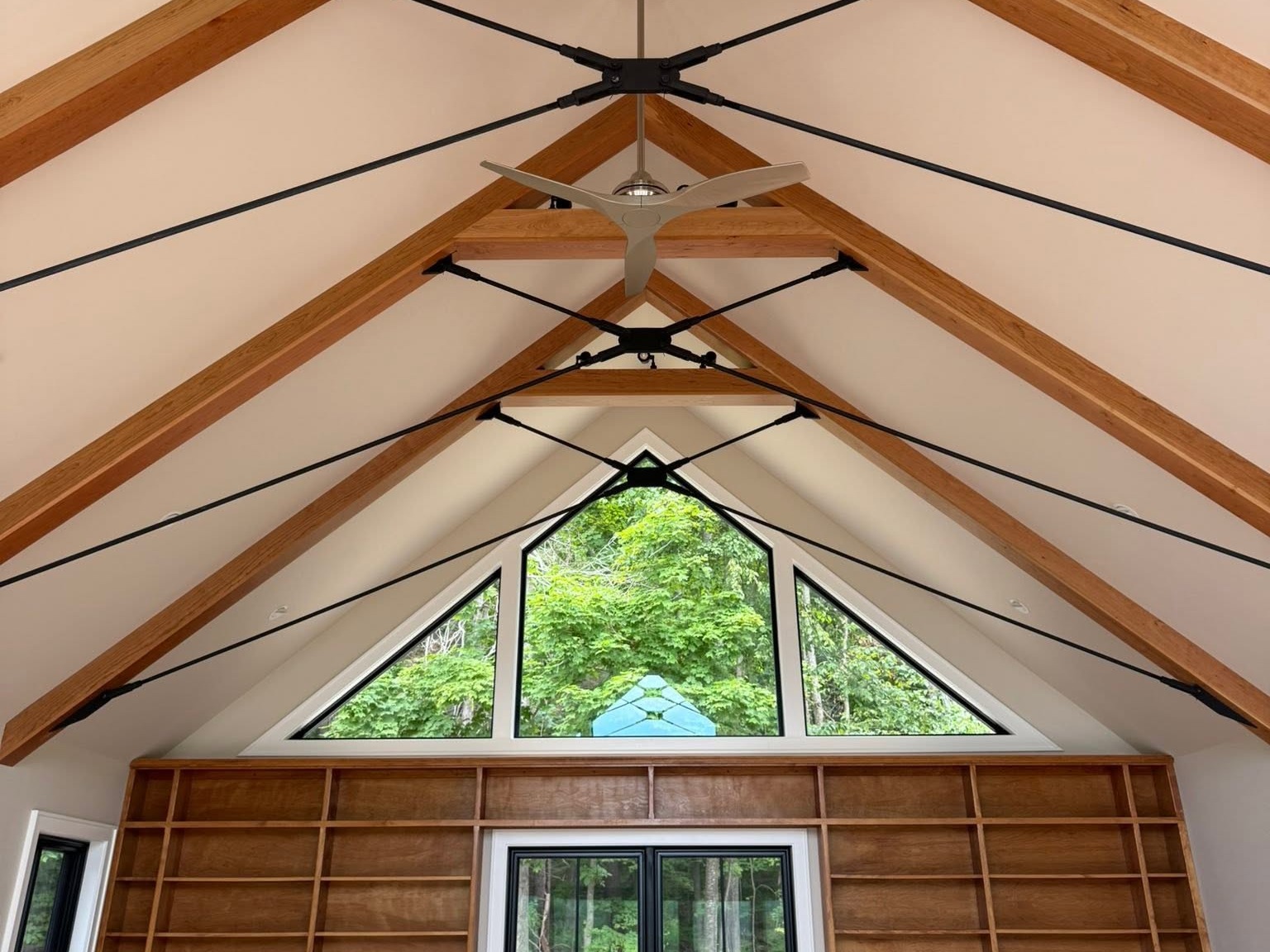 Exposed timber trusses and a ceiling fan installed beneath a vaulted farmhouse ceiling